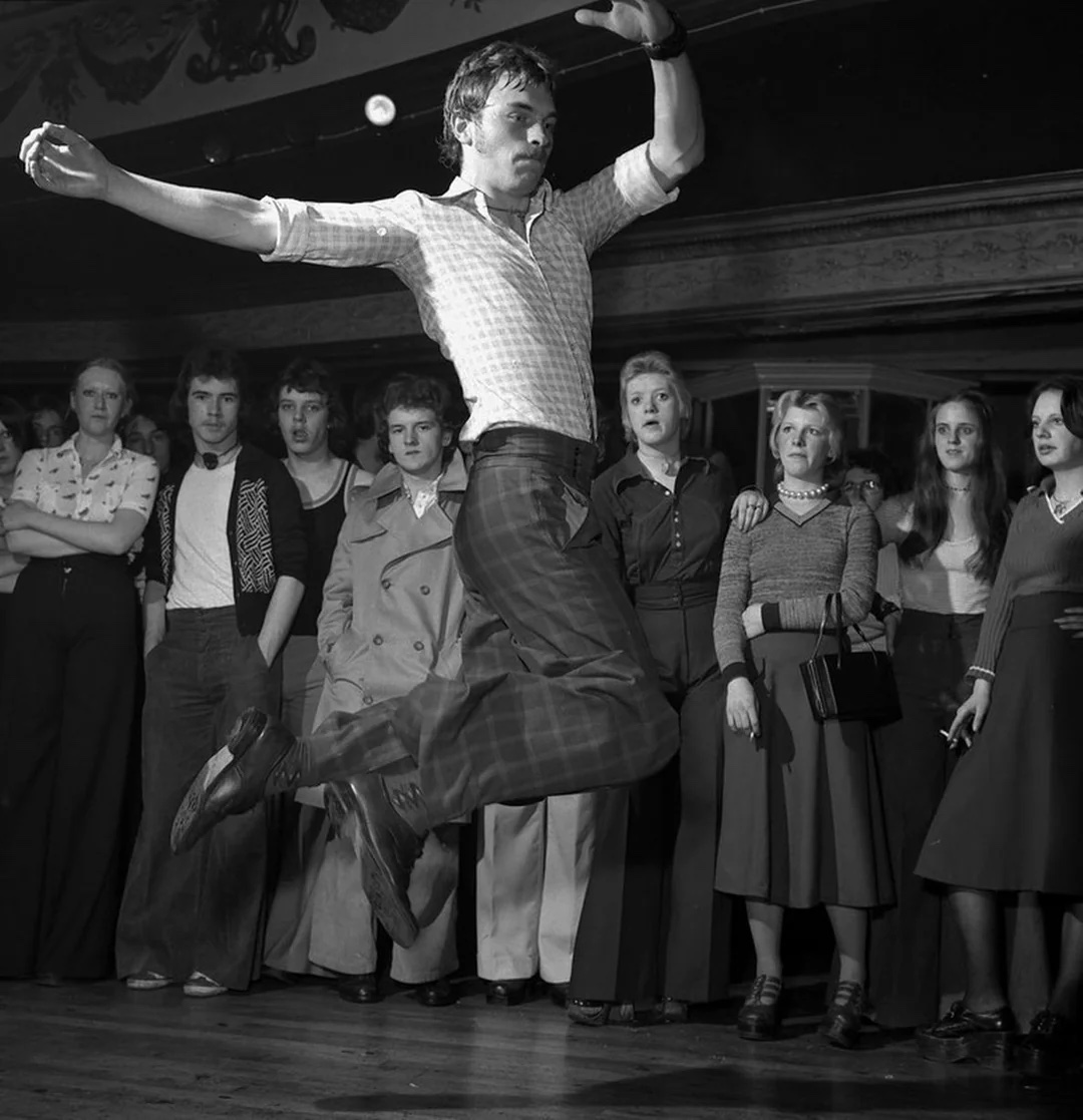 A man leaping in the air on a dance floor with a crowd watching